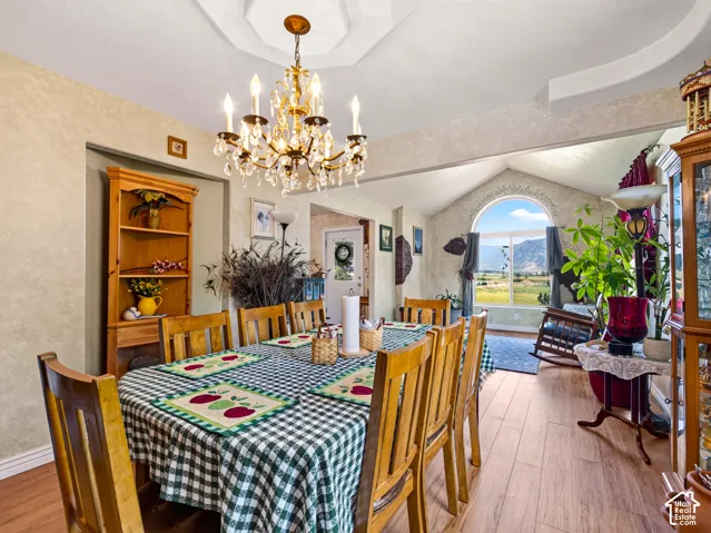 Formal dining area with tray ceiling, chandelier, LVP flooring, shelving, vaulted ceiling, and an arched window