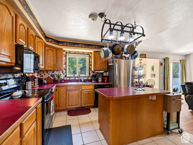 Kitchen featuring wood cabinetry, stainless steel refrigerator, black range, black microwave, and a pot rack with integrated lighting