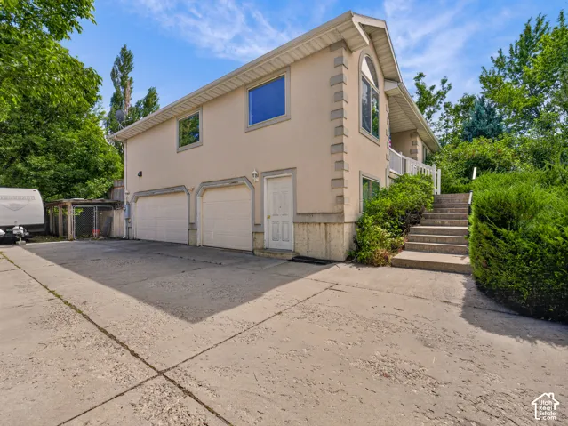 Three-car garage with arched accents, concrete driveway, and exterior staircase with railing
