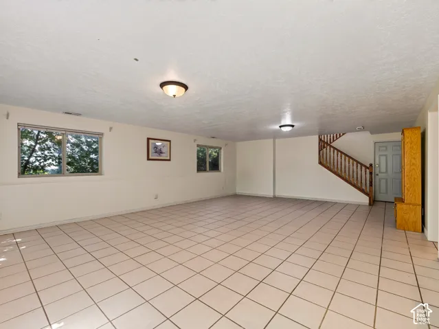 Spacious room featuring tile flooring, multiple windows, built-in wooden staircase, and overhead lighting fixtures