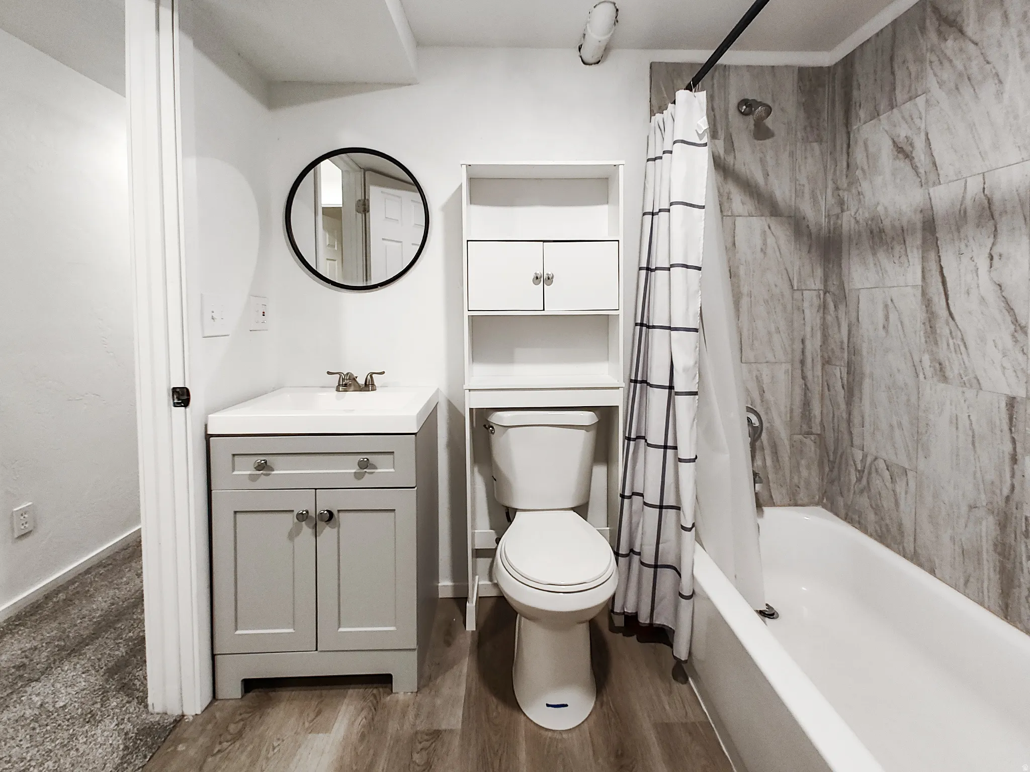 Wood-finish flooring, white vanity with integrated sink, toilet with built-in storage, and a bathtub with tile surround