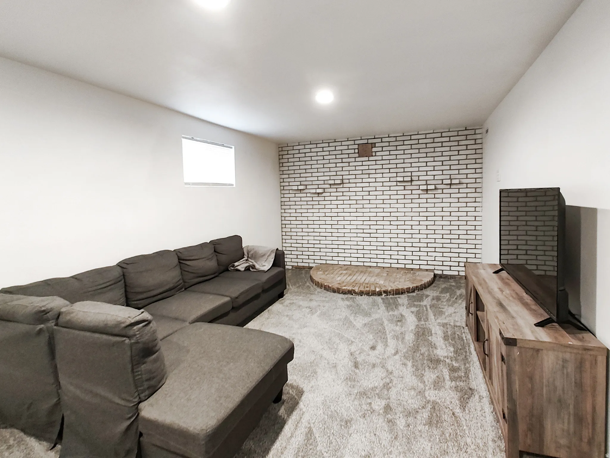 Recessed ceiling lighting, white painted brick accent wall, light-colored carpeting, and a wood-finish media console