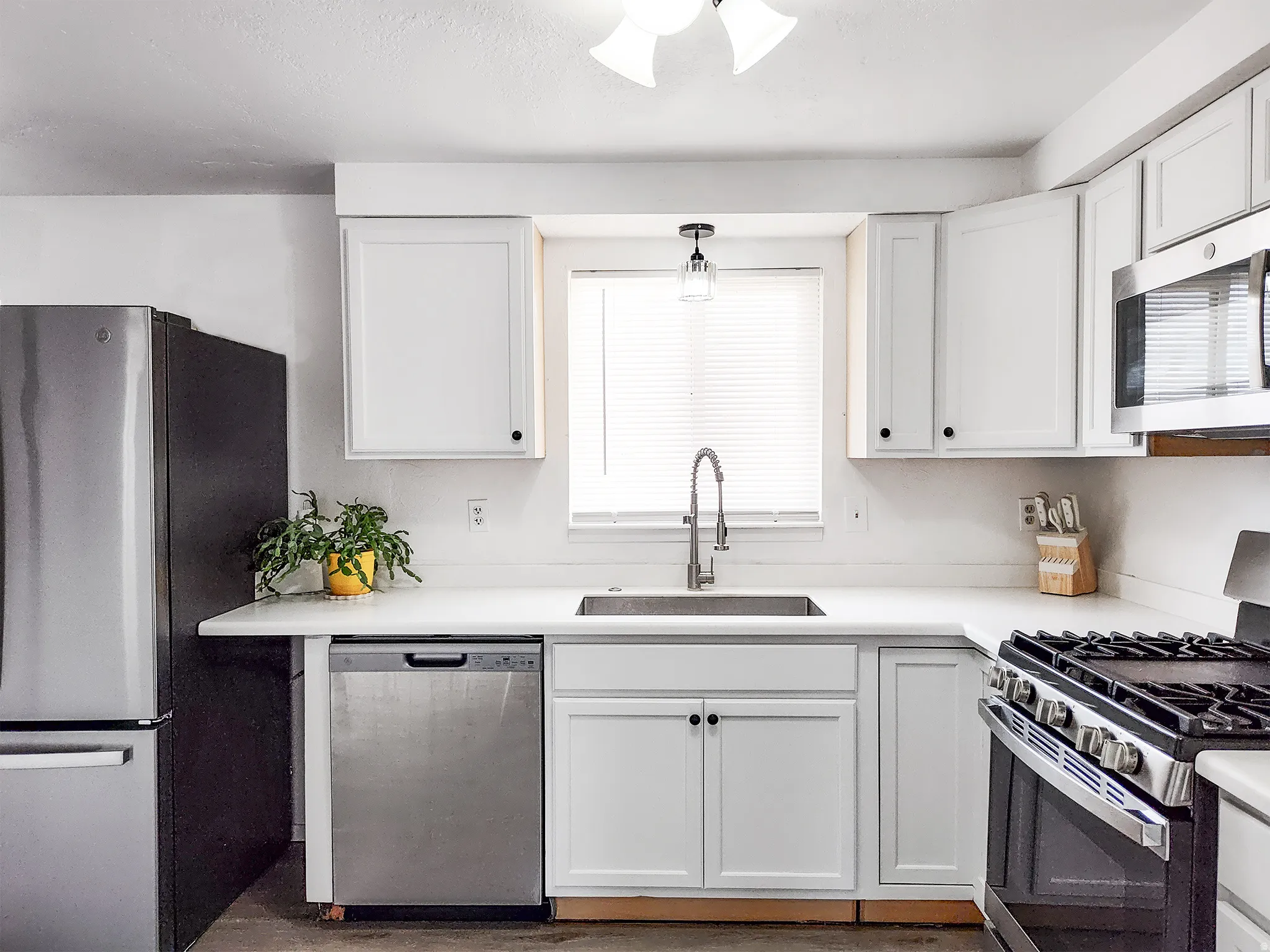 Kitchen featuring white cabinetry, light-toned countertops, a stainless steel sink with a gooseneck faucet, a stainless steel refrigerator, and a stainless steel range