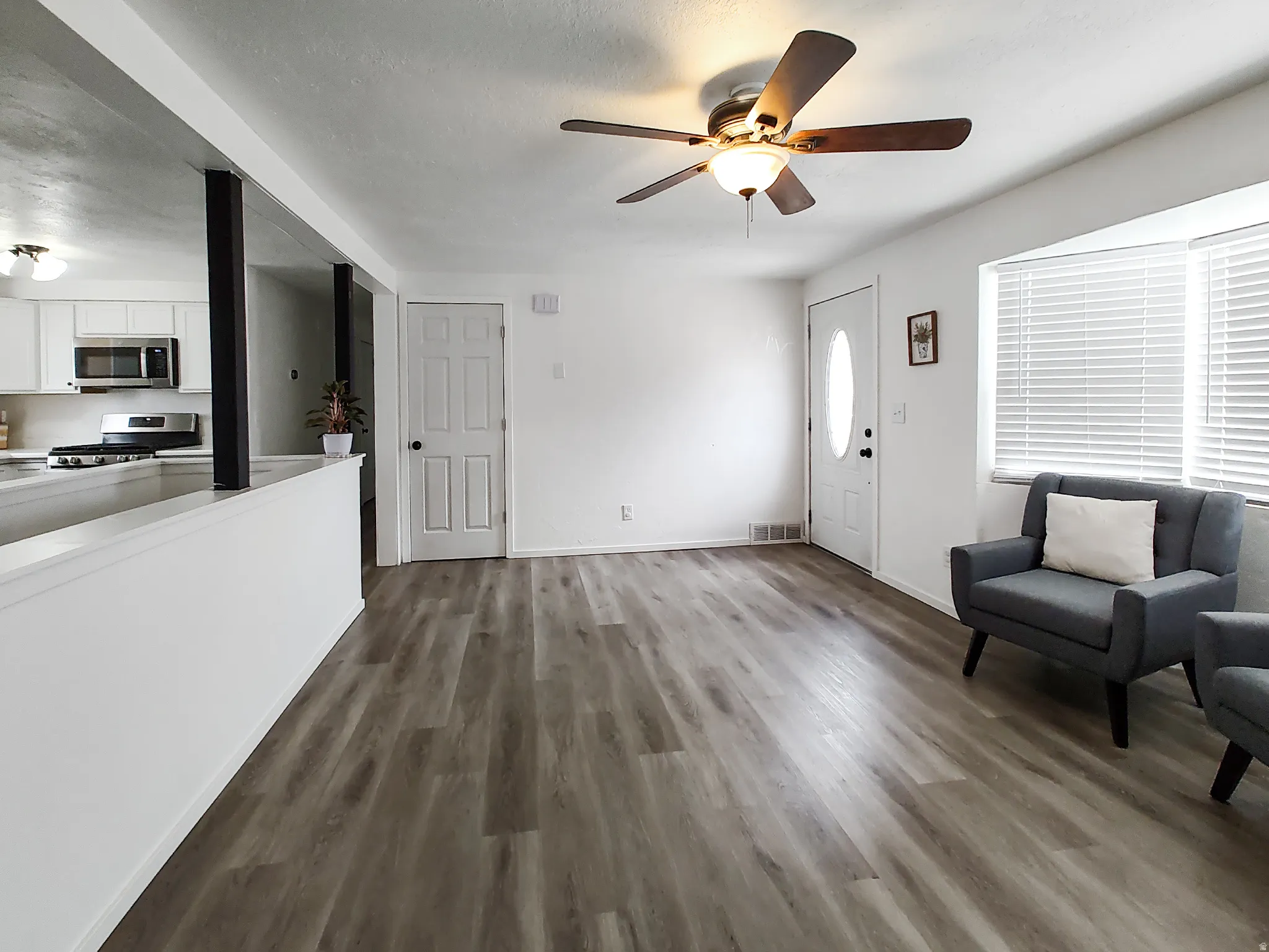 Wood-finish flooring, ceiling fan with light fixture, white interior walls, and bay window with blinds