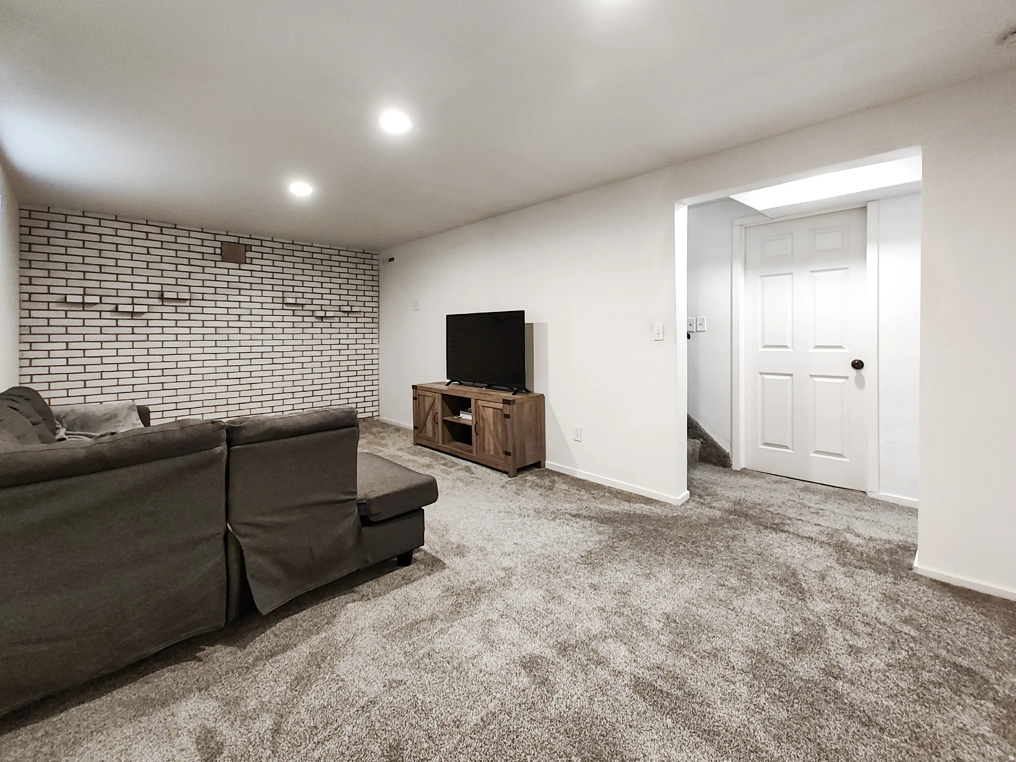 Recessed lighting, white painted brick accent wall, white interior door, and grey carpet flooring