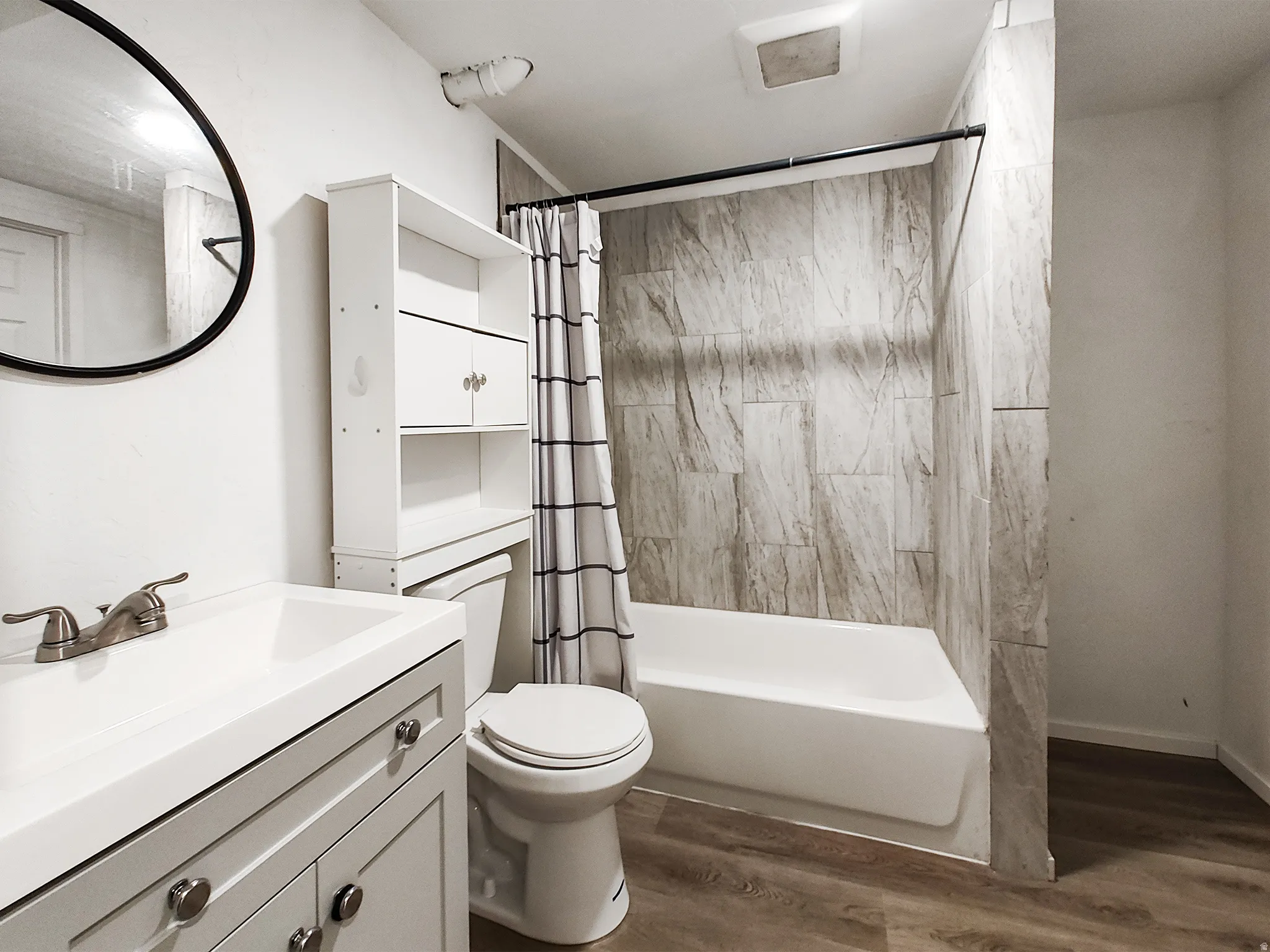Bathroom featuring a vanity with an integrated sink, brushed nickel faucet, wood-finish flooring, a toilet, and a shower/tub combination with patterned tile surround