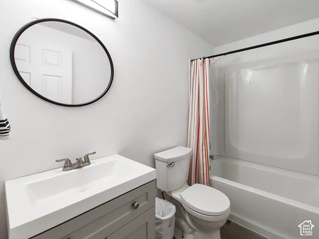 White walls, a white integrated sink, a gray vanity cabinet with silver hardware, a black-framed circular mirror, and a white bathtub with a shower