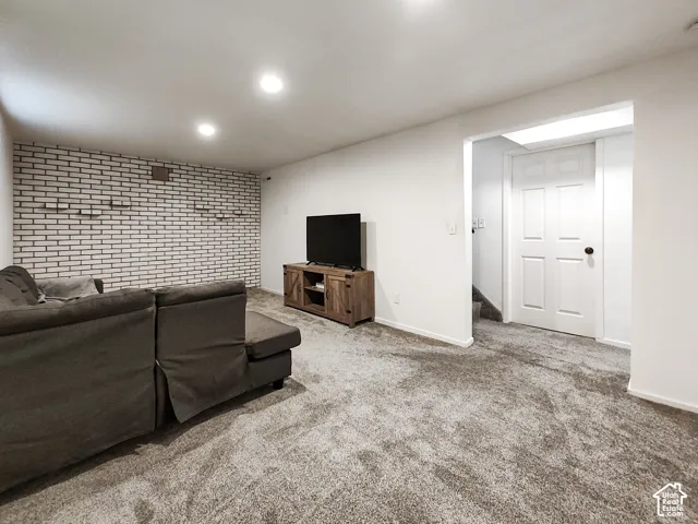 Recessed lighting, white painted brick accent wall, white interior door, and grey carpet flooring