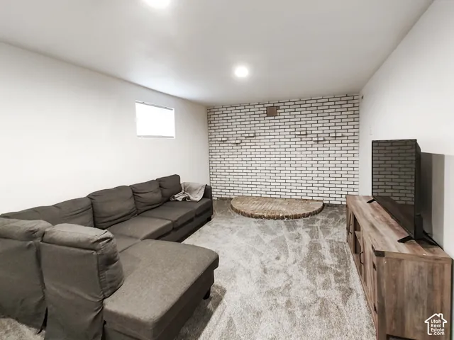 Recessed ceiling lighting, white painted brick accent wall, light-colored carpeting, and a wood-finish media console