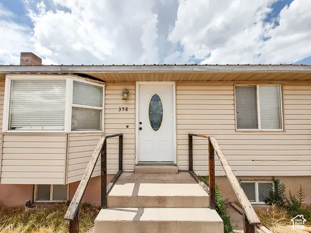 Welcoming front elevation featuring a centered entry door with decorative oval window, dual concrete steps with sturdy railings, horizontal vinyl siding, and large multi-pane windows allowing abundant natural light