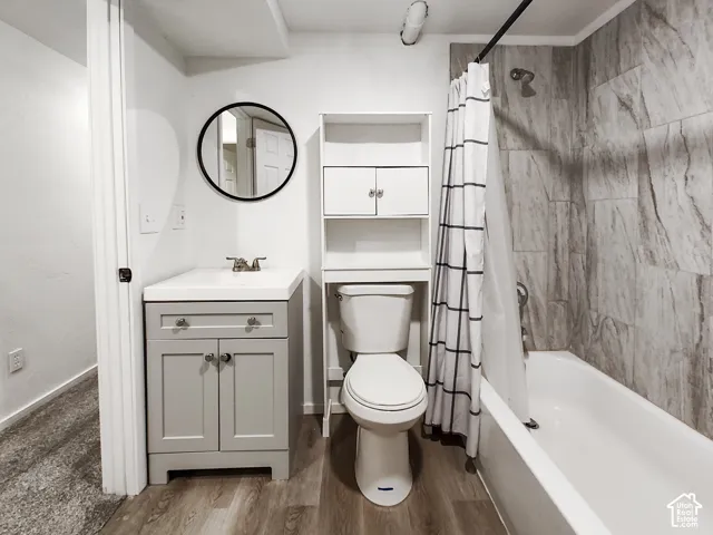 Wood-finish flooring, white vanity with integrated sink, toilet with built-in storage, and a bathtub with tile surround