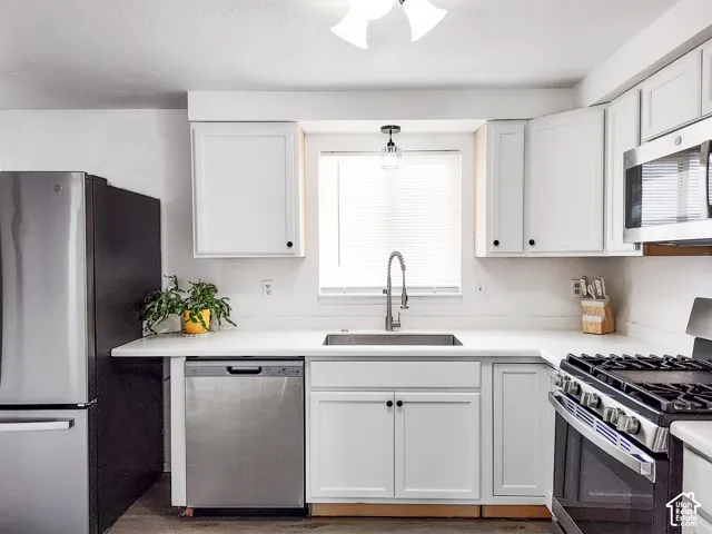 Kitchen featuring white cabinetry, light-toned countertops, a stainless steel sink with a gooseneck faucet, a stainless steel refrigerator, and a stainless steel range