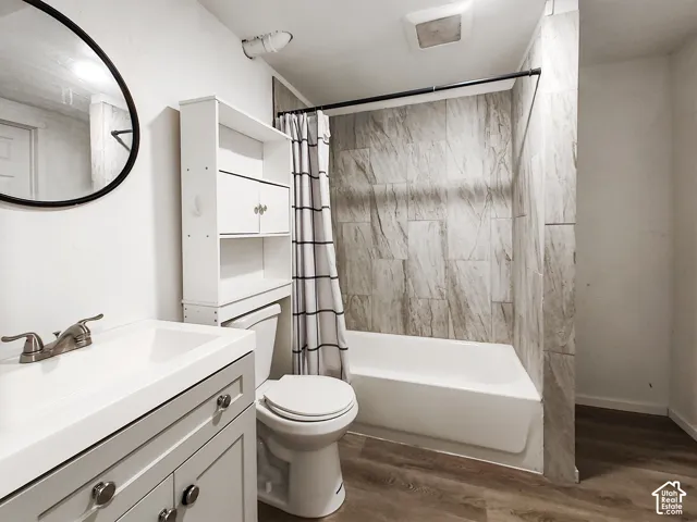Bathroom featuring a vanity with an integrated sink, brushed nickel faucet, wood-finish flooring, a toilet, and a shower/tub combination with patterned tile surround