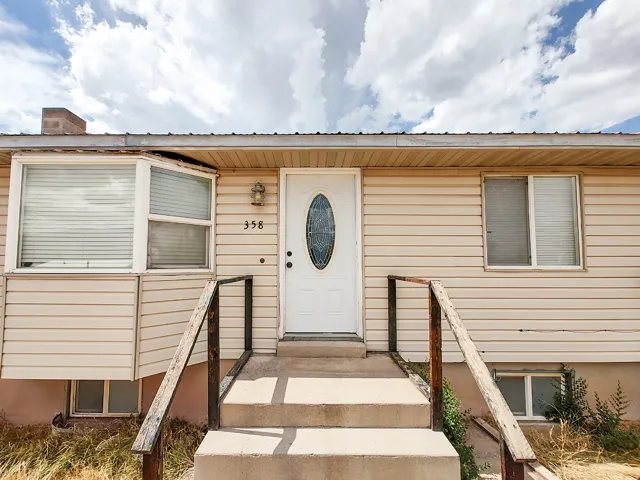 Welcoming front elevation featuring a centered entry door with decorative oval window, dual concrete steps with sturdy railings, horizontal vinyl siding, and large multi-pane windows allowing abundant natural light