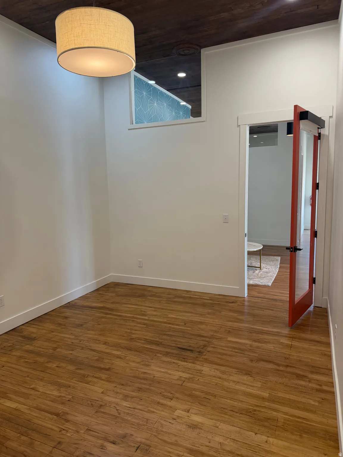 Wood-finish flooring, white walls, dark wood-paneled ceiling, and a fabric drum pendant light