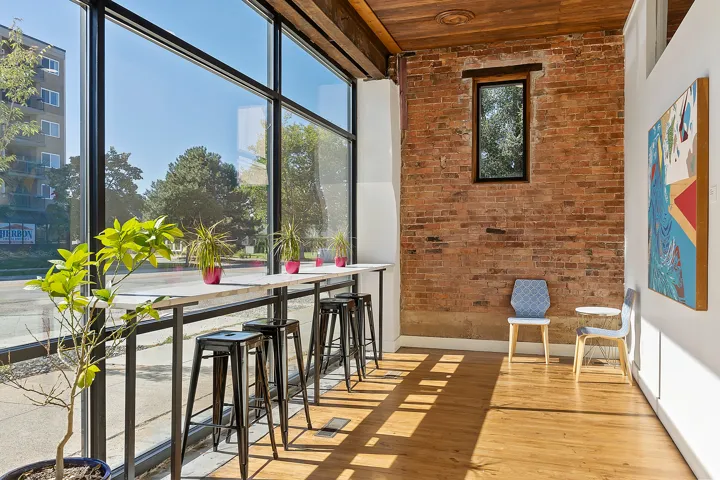 Expansive floor-to-ceiling windows, exposed brick wall, wood-finish flooring, wood plank ceiling, and a built-in counter