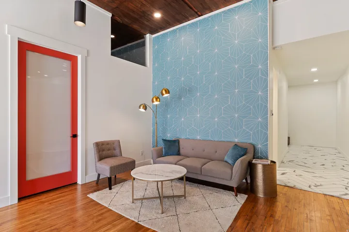 Hardwood flooring, vibrant red door with frosted glass panel, recessed lighting, and a unique accent wall with geometric pattern
