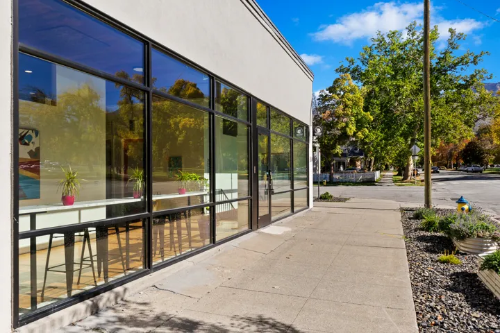 Full-height storefront windows with dark frames, a white facade, and a concrete sidewalk