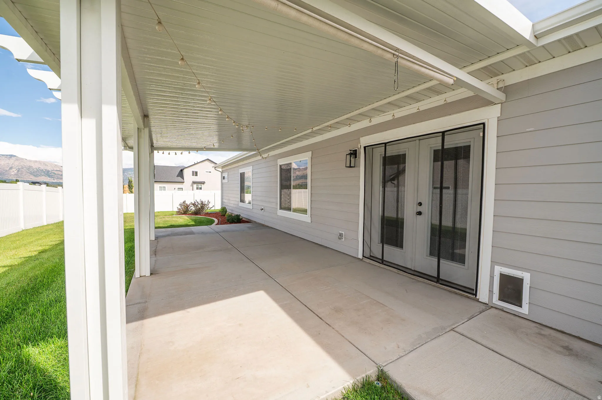 Covered patio with concrete flooring, white support columns, and an exterior wall light fixture