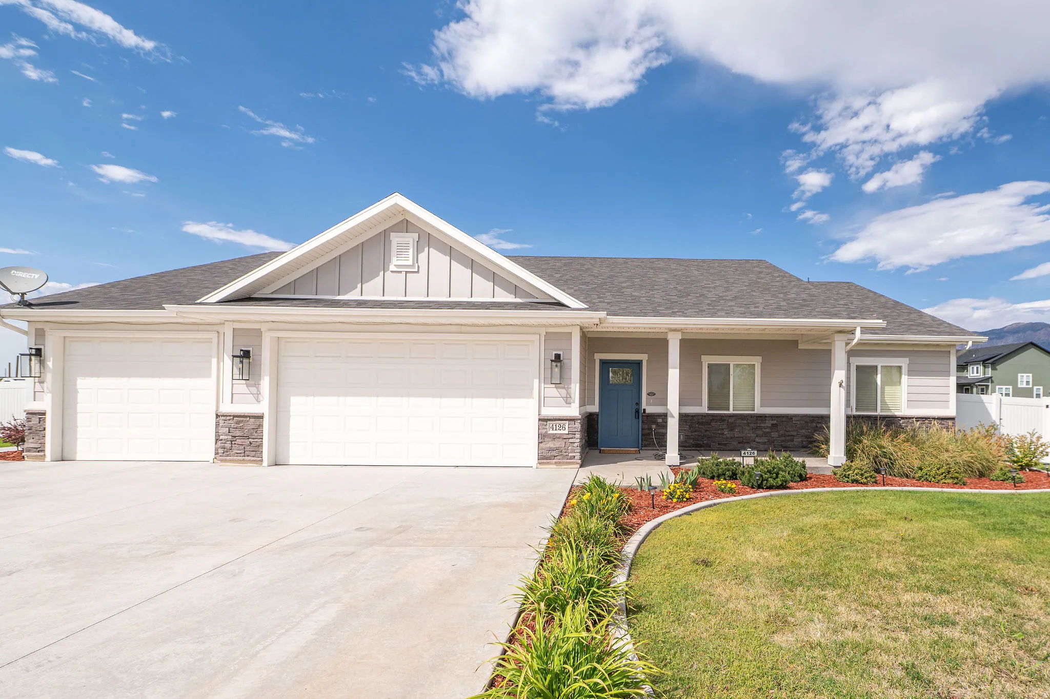 Siding exterior with stone accents, a three-car garage, a covered entry, and a landscaped front yard with a concrete driveway