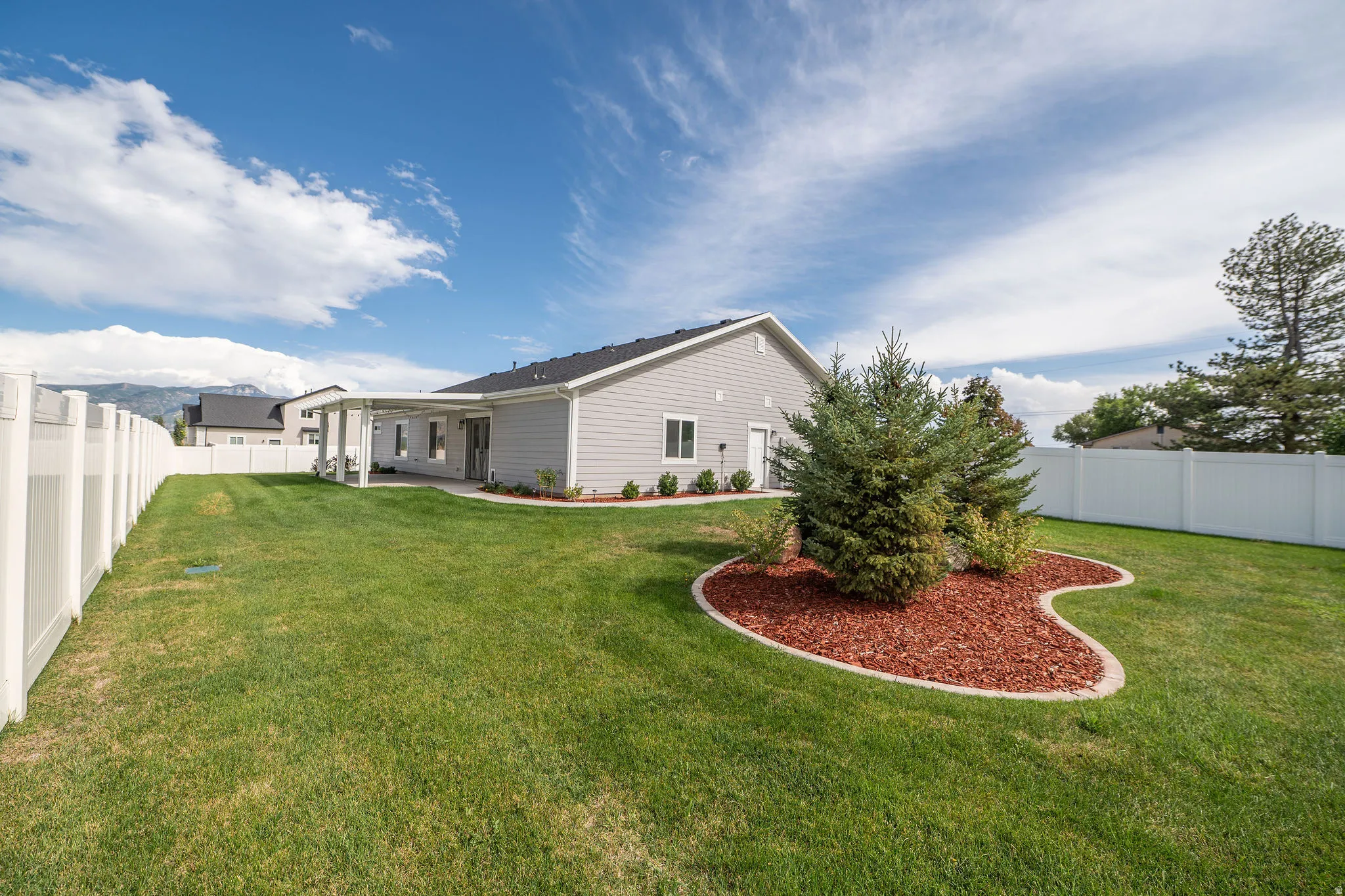 Expansive backyard with a covered patio, vinyl fencing, manicured lawn, and a landscaped garden bed