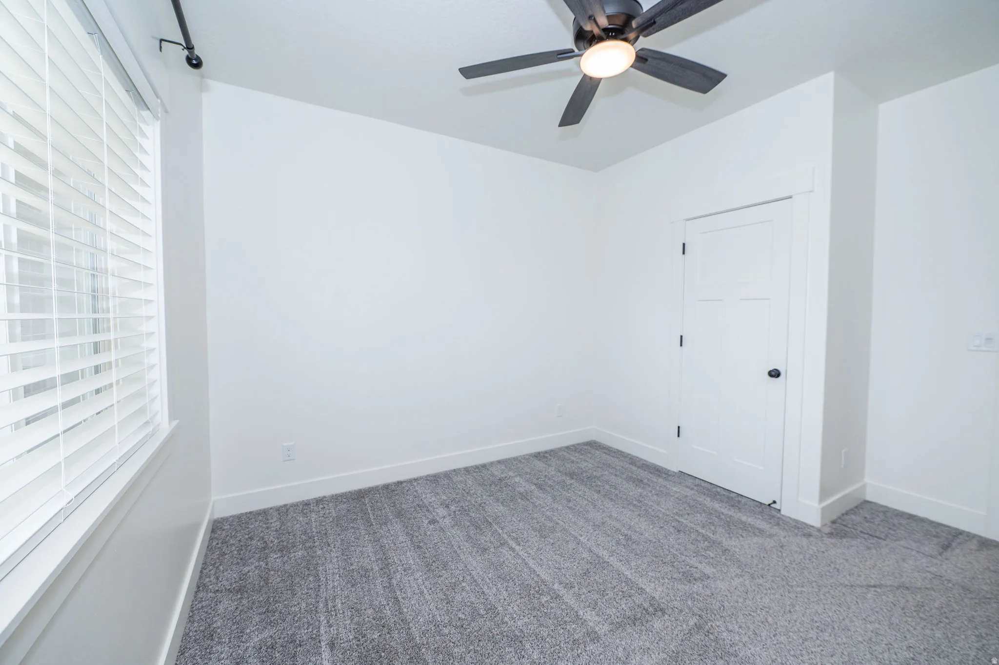 Room featuring white walls, gray carpeting, a dark ceiling fan with integrated lighting, and a white paneled door