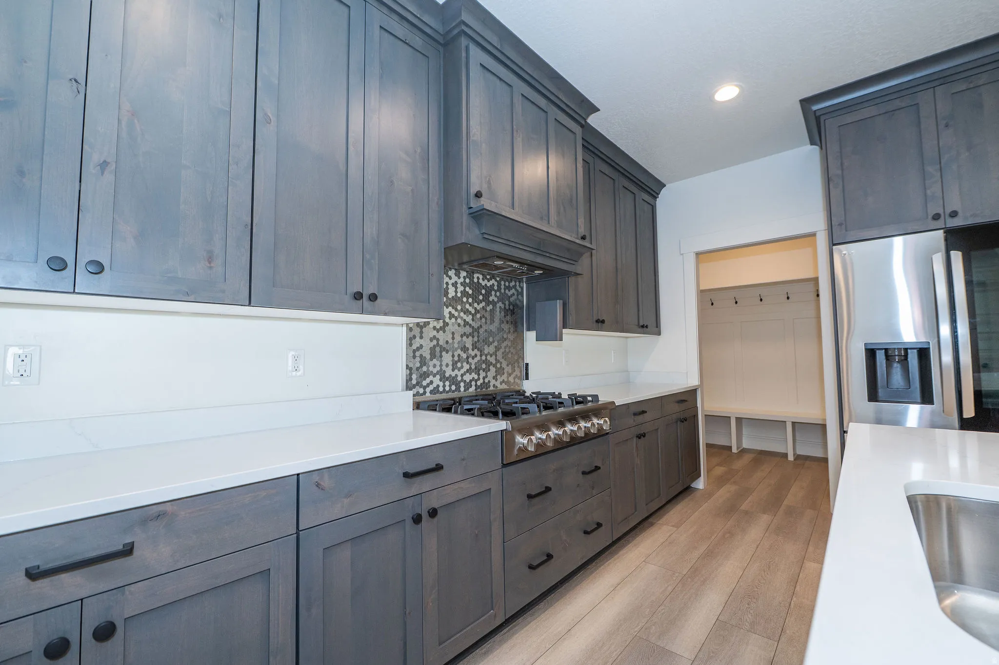 Gray wood-finish cabinetry, white countertops, built-in stainless steel appliances, mosaic tile backsplash, and wood-finish flooring