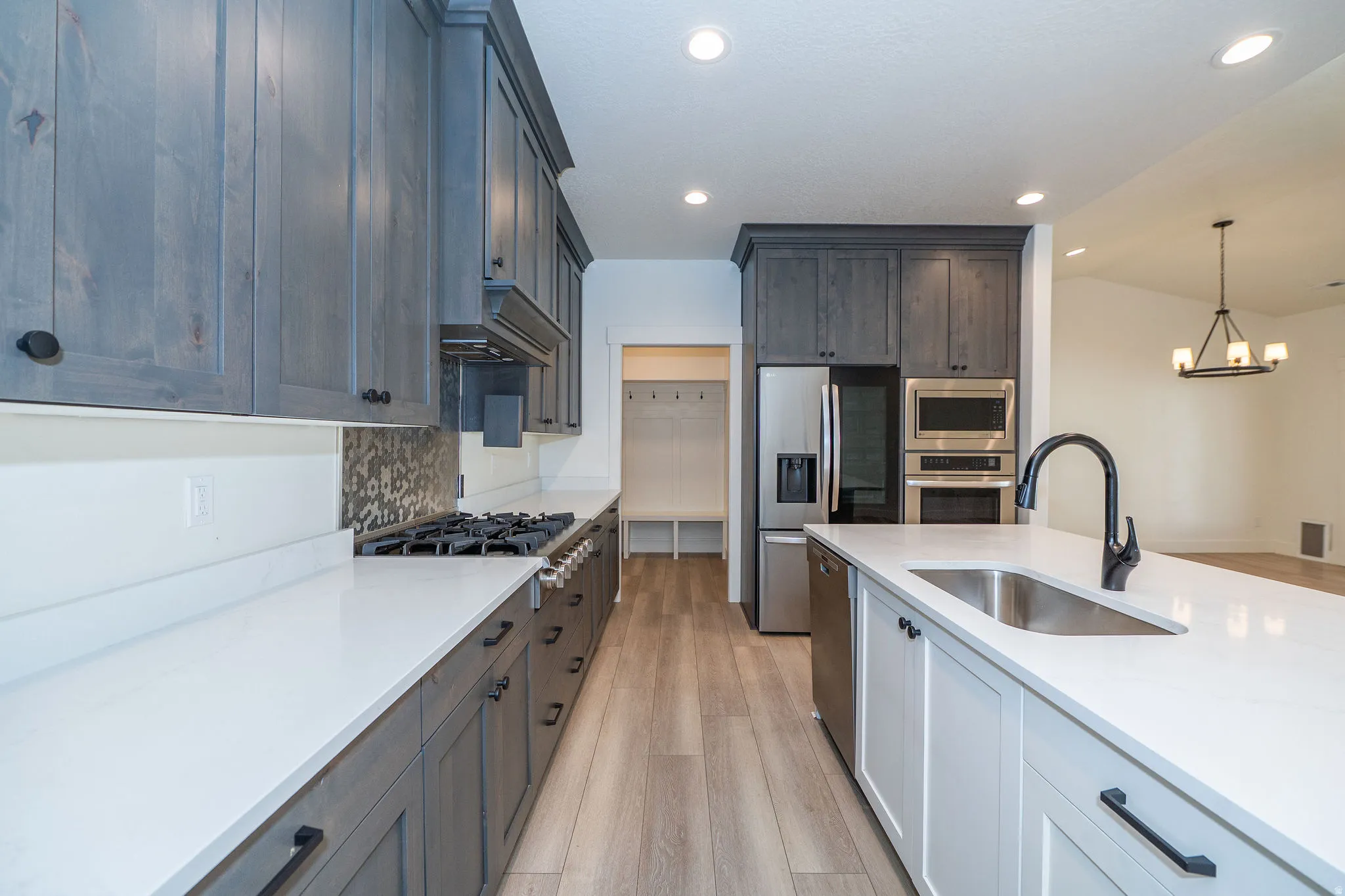 Kitchen featuring gray cabinetry, white countertops, built-in stainless steel appliances, and a central island with an undermount sink and matte black faucet