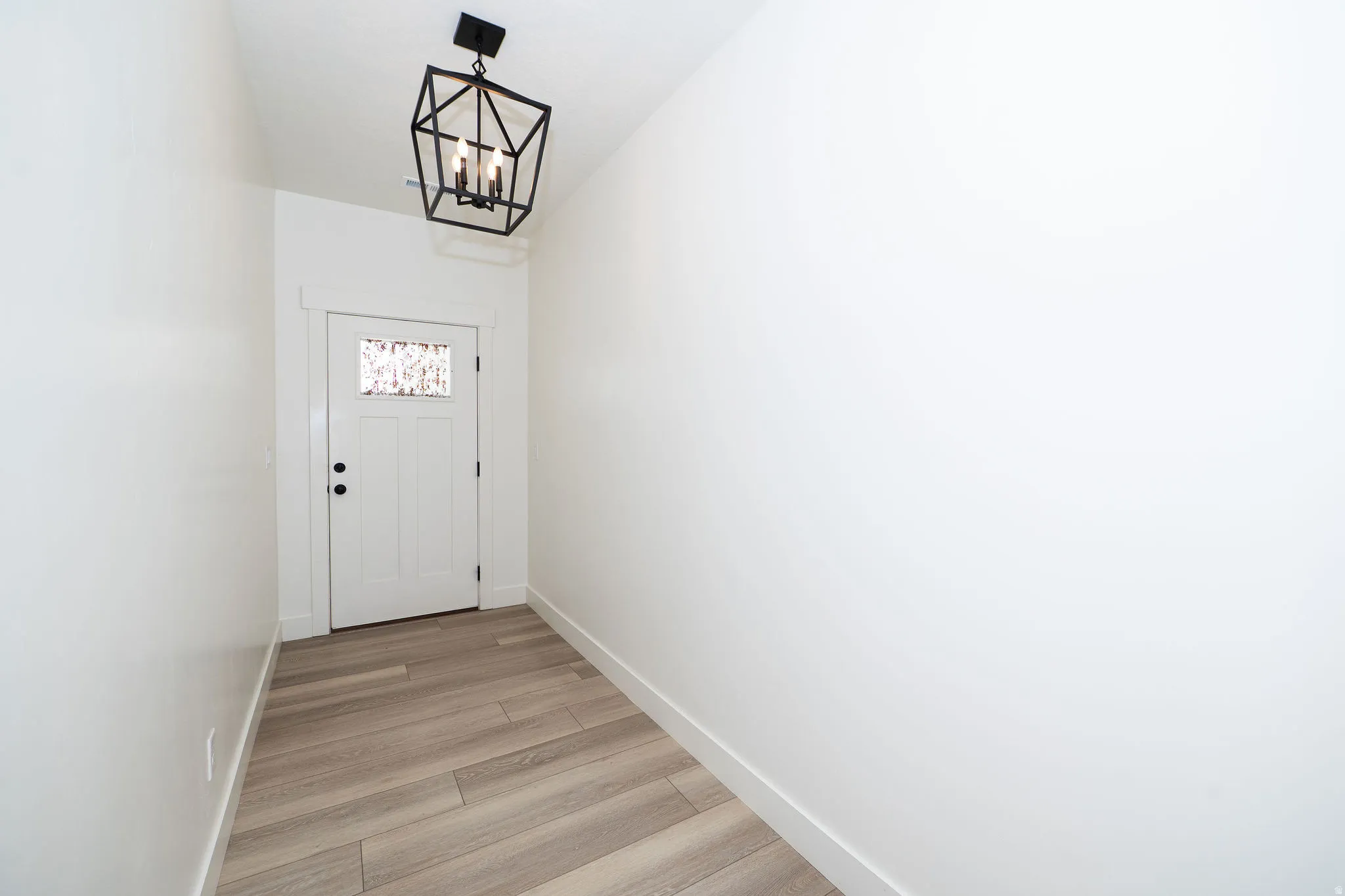 Entryway with wood-finish flooring, a white paneled door with decorative glass inlay, and a contemporary geometric light fixture