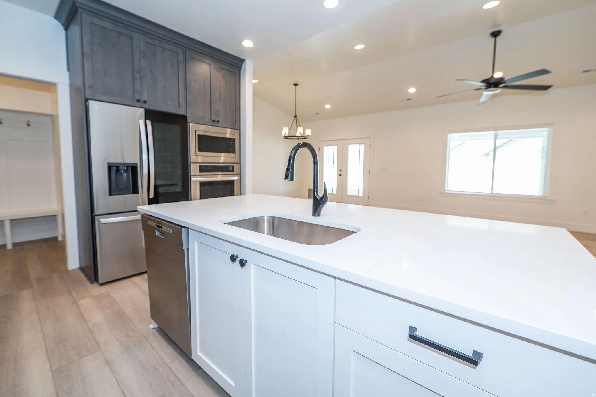 Kitchen island with a stainless steel sink and matte black faucet, integrated stainless steel dishwasher, and white cabinetry with dark hardware