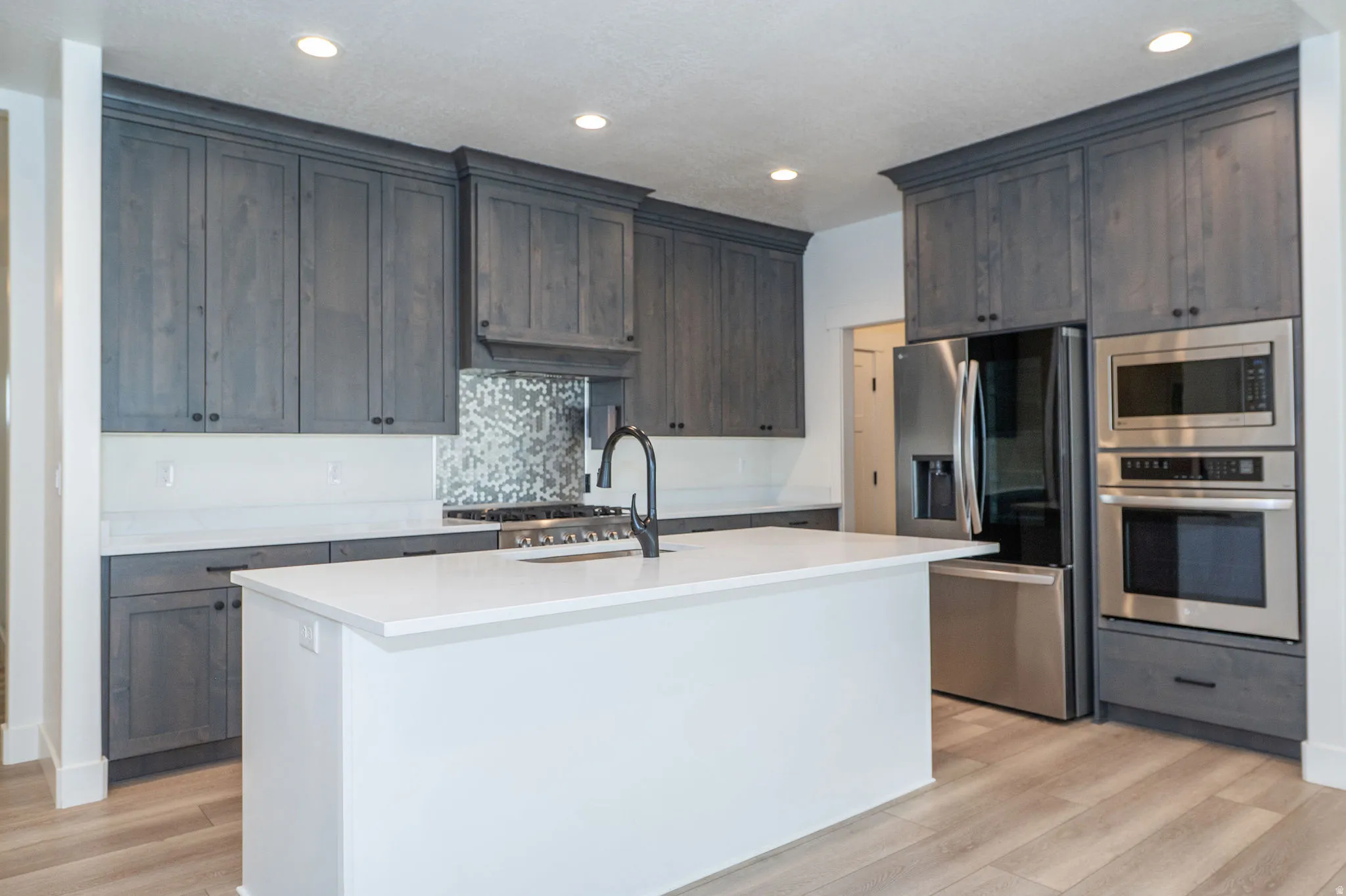 Kitchen featuring grey cabinetry, stainless steel appliances, a center island with a white countertop, and wood-finish flooring