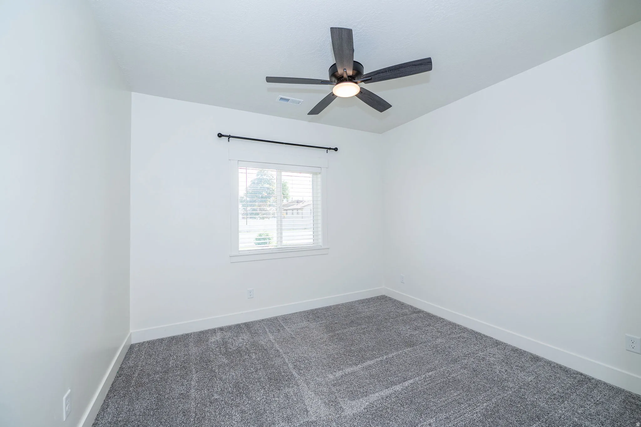 Recessed window with white blinds, dark gray carpet, contemporary ceiling fan with integrated lighting, and a dark curtain rod