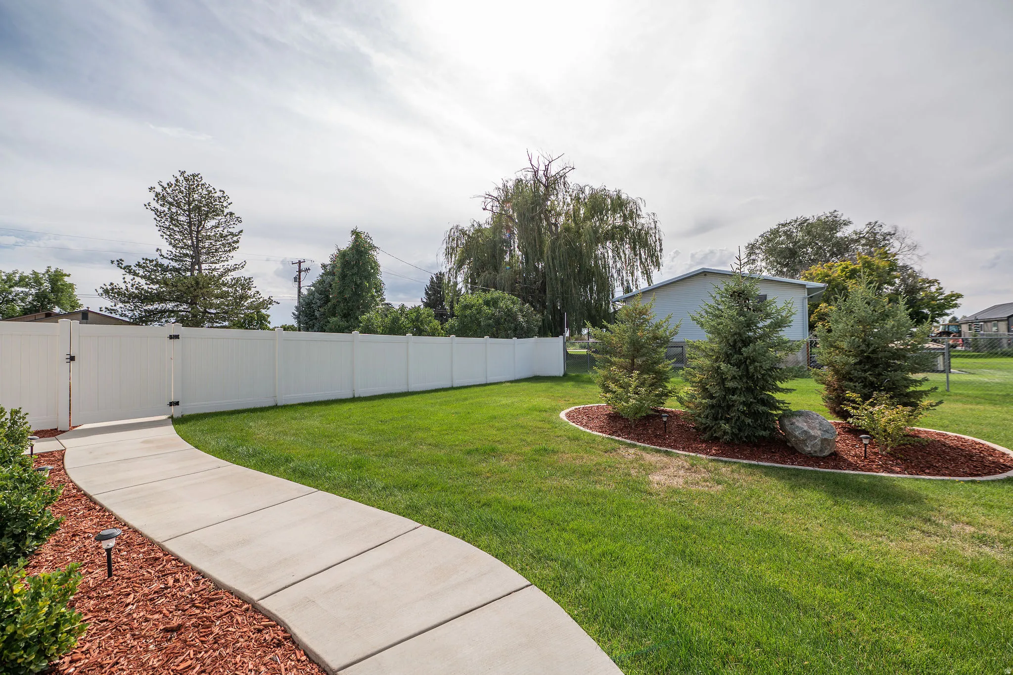 Manicured lawn with a curved concrete pathway and a white privacy fence