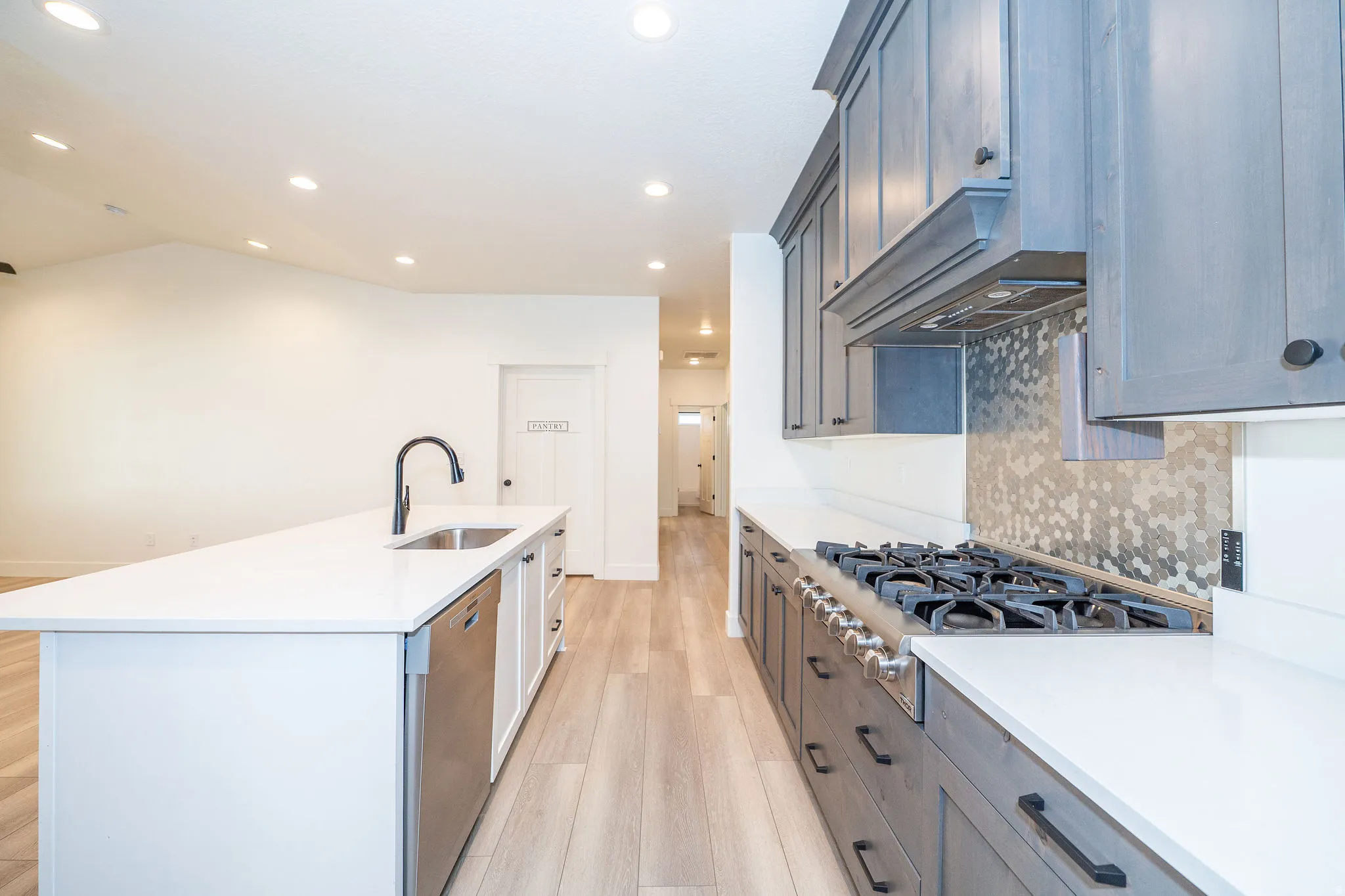 Kitchen featuring recessed lighting, a large island with a stainless steel sink and matte black faucet, wood-finish flooring, white countertops, and a hexagon-patterned backsplash