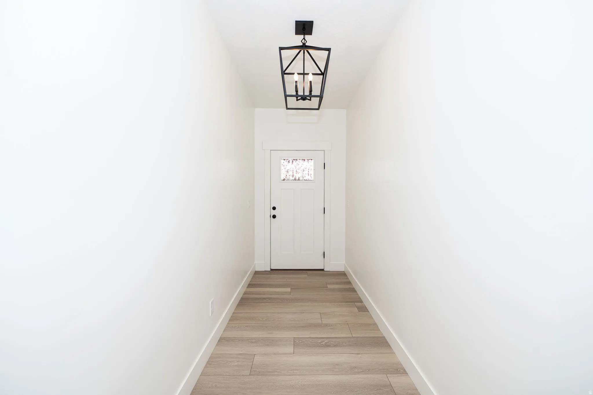 Entryway featuring wood-finish flooring, a contemporary black metal lantern pendant light, and a white paneled door with decorative glass inserts