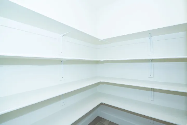 Corner pantry featuring multiple white shelves and wood-finish flooring