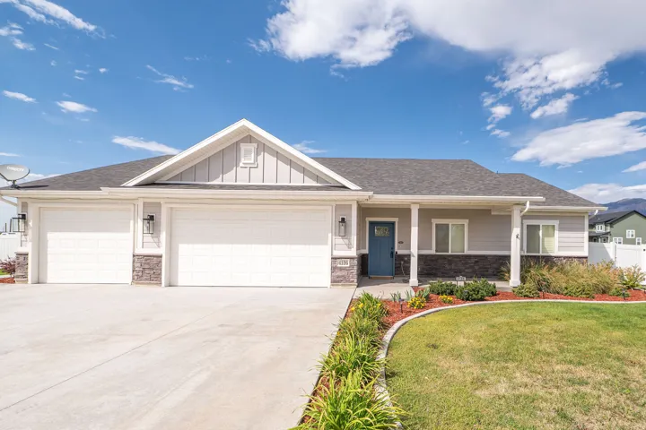 Siding exterior with stone accents, a three-car garage, a covered entry, and a landscaped front yard with a concrete driveway