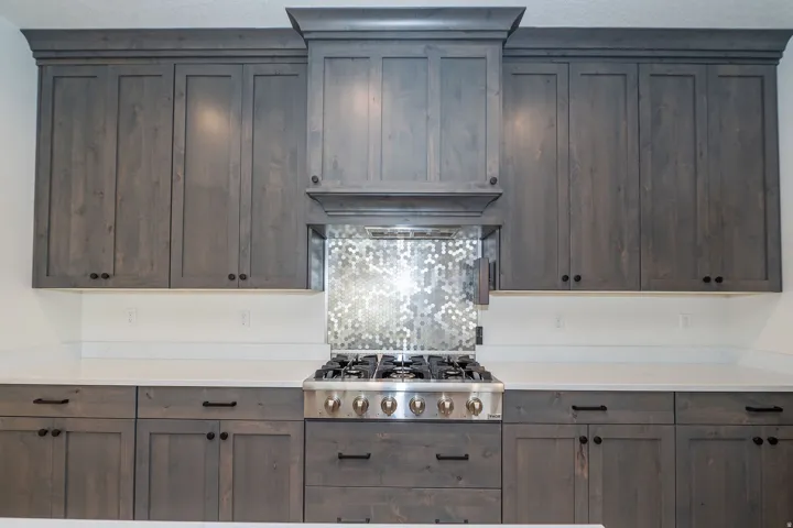 Gray wood-finish cabinetry, white countertops, built-in range hood, stainless steel gas range, and mosaic tile backsplash