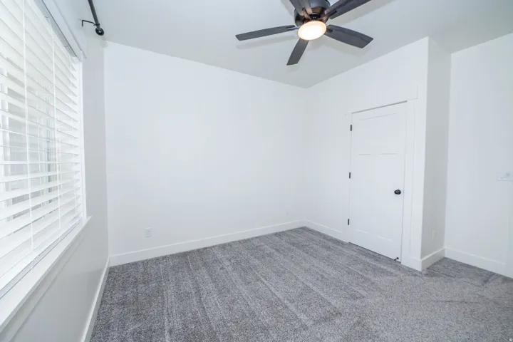 Room featuring white walls, gray carpeting, a dark ceiling fan with integrated lighting, and a white paneled door