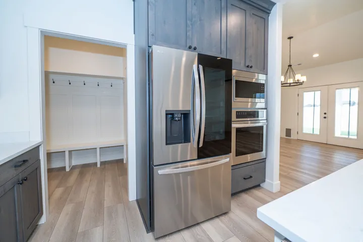 Stainless steel refrigerator, built-in microwave, wall oven, wood-finish flooring, and a built-in mudroom bench with coat hooks