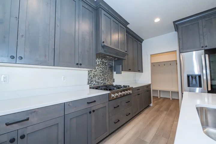 Gray wood-finish cabinetry, white countertops, built-in stainless steel appliances, mosaic tile backsplash, and wood-finish flooring