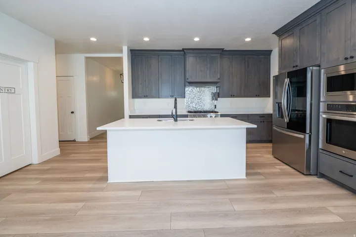 Spacious kitchen featuring a central island with a white countertop, wood-finish flooring, dark wood cabinetry, and stainless steel appliances