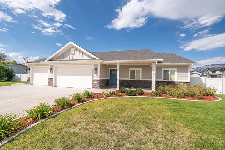Pitched roofline with gray shingles, two-car garage, stone and siding exterior, covered porch entry, and a well-maintained front lawn