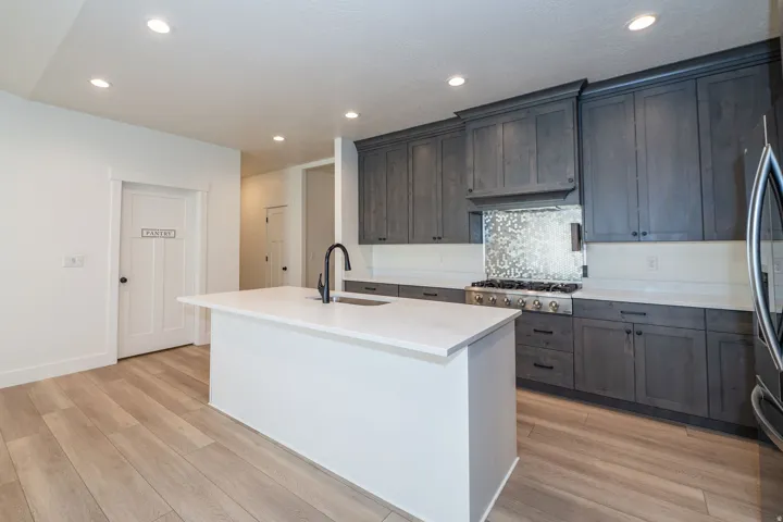Recessed lighting illuminates the kitchen featuring a central island, a built-in range, a patterned backsplash, and dark wood-finish cabinetry