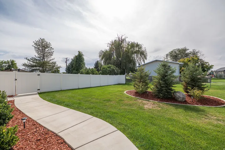 Manicured lawn with a curved concrete pathway and a white privacy fence