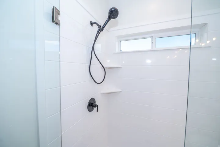Walk-in shower with clear glass enclosure, matte black shower fixtures, two built-in corner shelves, and a horizontal window