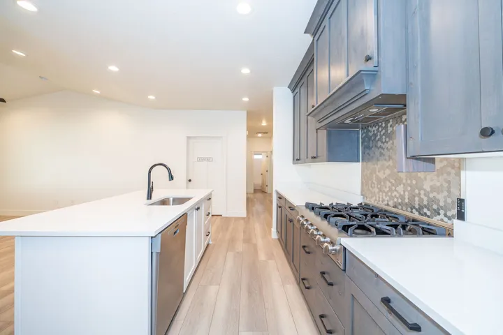 Kitchen featuring recessed lighting, a large island with a stainless steel sink and matte black faucet, wood-finish flooring, white countertops, and a hexagon-patterned backsplash