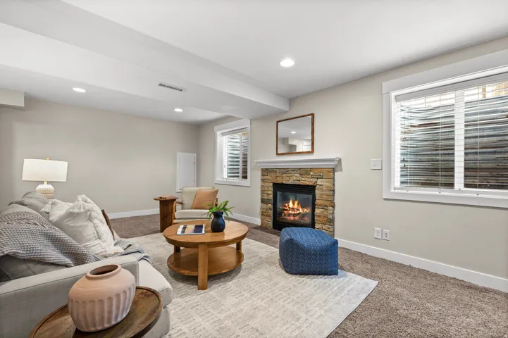 Stone-faced fireplace with a white mantel, recessed lighting, and carpeted flooring