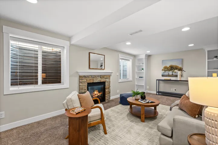 Stone-clad fireplace, recessed lighting, built-in shelving, windows with white trim, and neutral-toned carpet