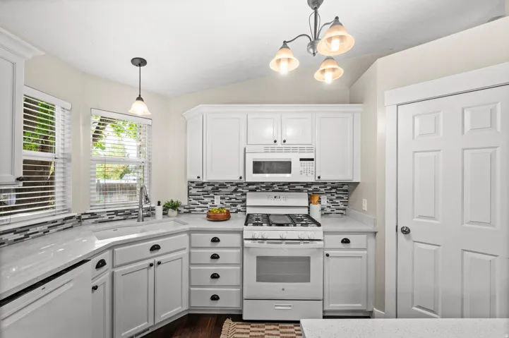White cabinetry with dark hardware, stone countertops, a mosaic tile backsplash, and stainless steel appliances
